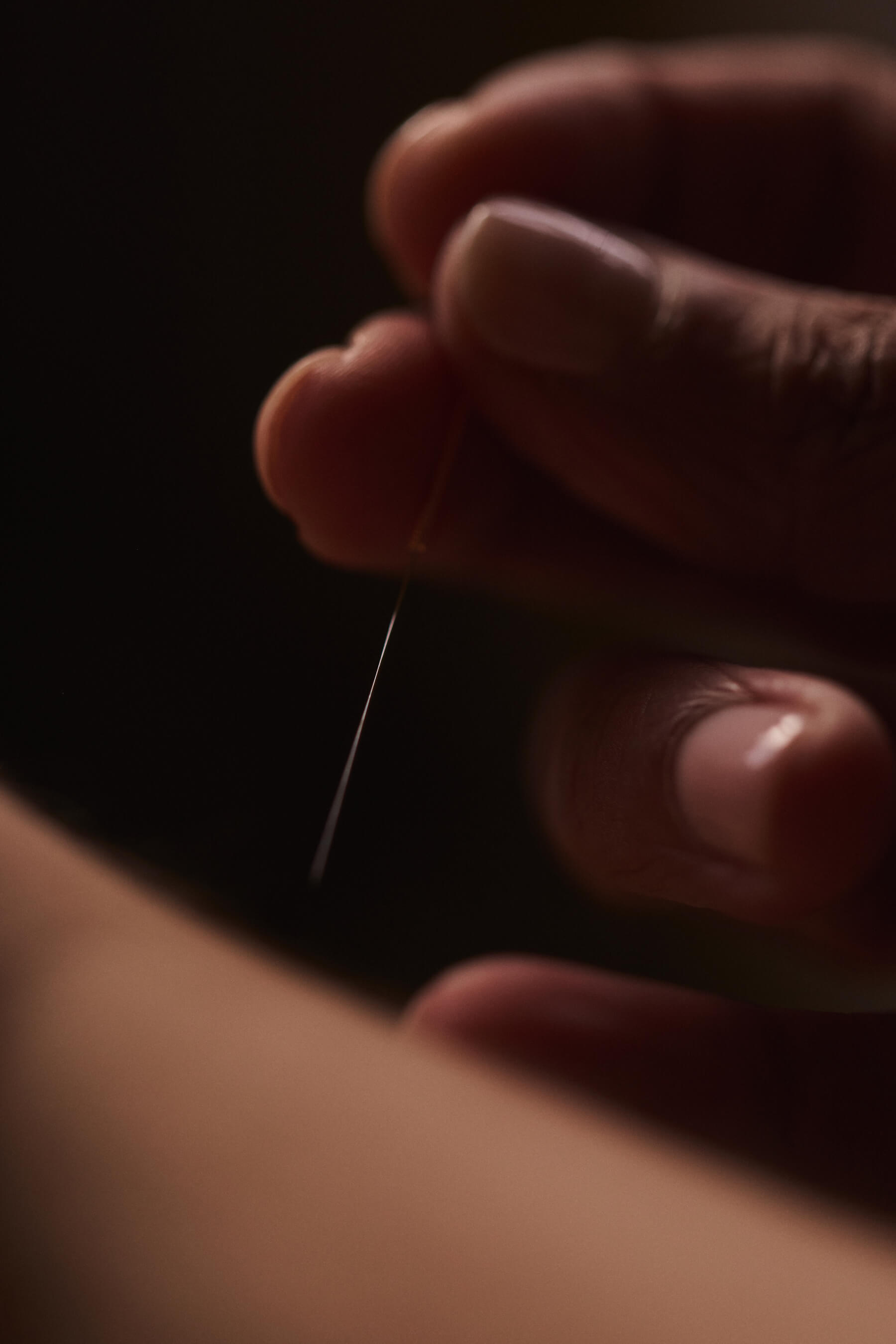 Close-up of a hand holding a fine acupuncture needle above the skin.