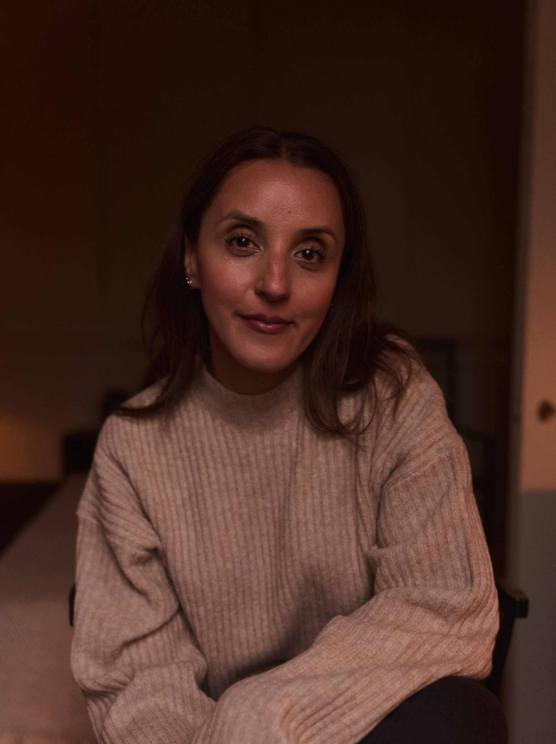Woman, wearing a beige sweater looking relaxed and friendly straight on into the camera. Her hair loosly laying on her shoulders.