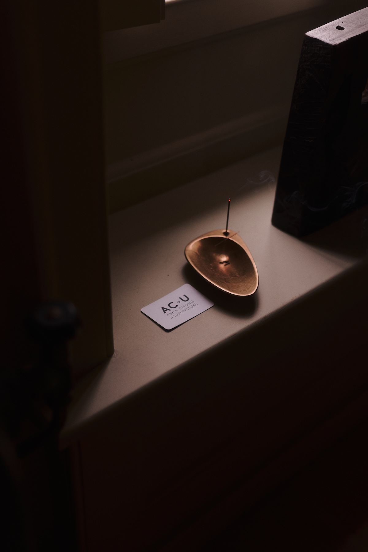 A small insense bowl on the windowsill, next to it a white business card of Asha Chong Acupuncture.